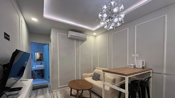 A modern living room with a wooden dining table, a sofa, and a coffee table. There is an air conditioning unit on the wall and a chandelier above the table. - Casanova (Batam)