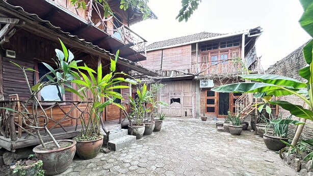 A courtyard with hexagonal stone paving, surrounded by wooden buildings with balconies and potted plants. - Chez Laelik (Sewon)