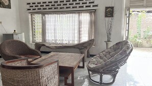 A room with a wooden table, two wicker chairs, a cushioned chair, a potted plant, and a window with curtains. - Chez Laelik (Sewon)