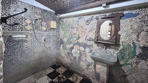 A bathroom with mosaic tile walls, a checkered floor, a wooden ceiling, and a stone sink. - Chez Laelik (Sewon)