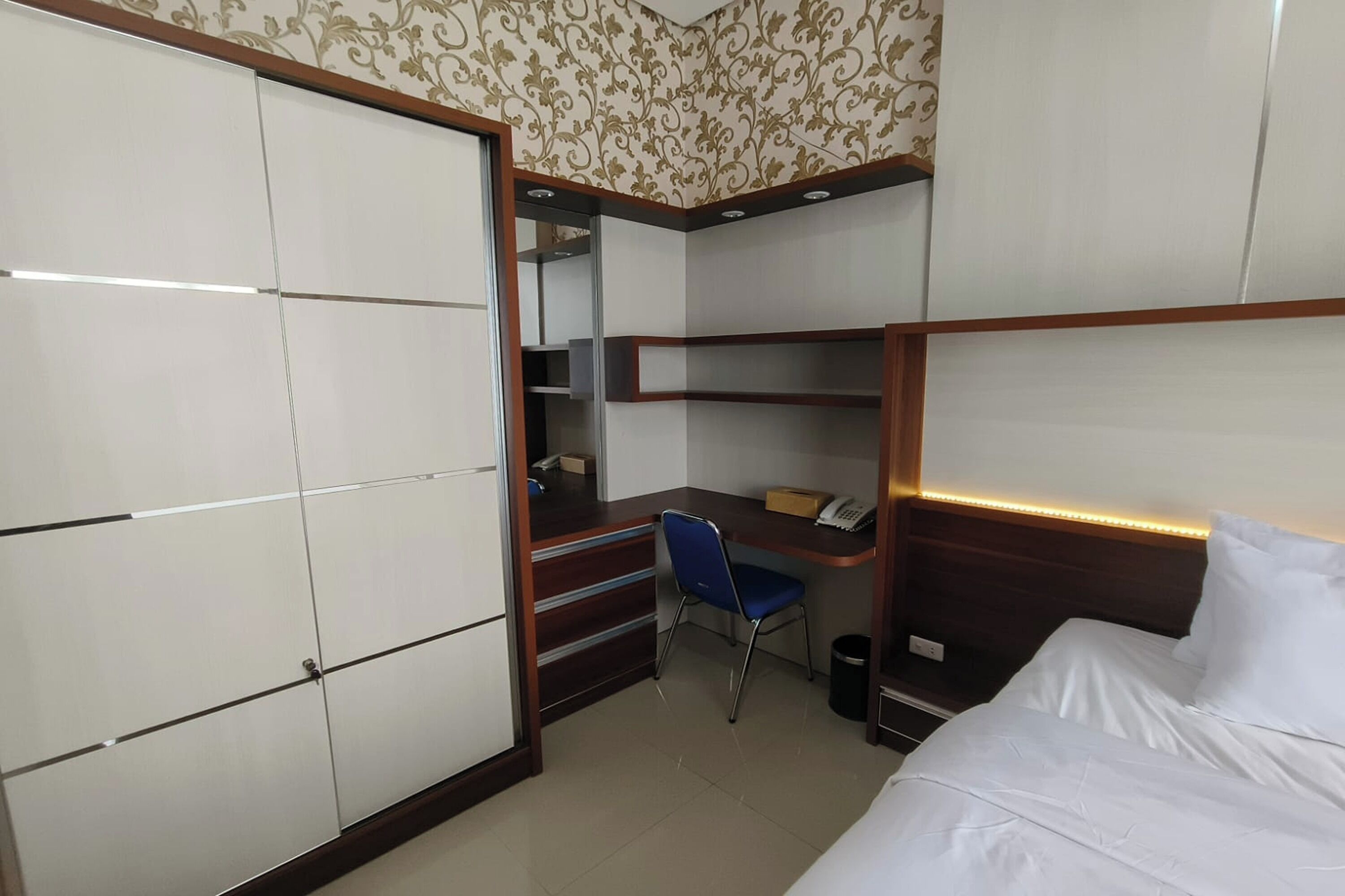 A compact hotel room with a bed, a desk, a chair, and a wardrobe.
