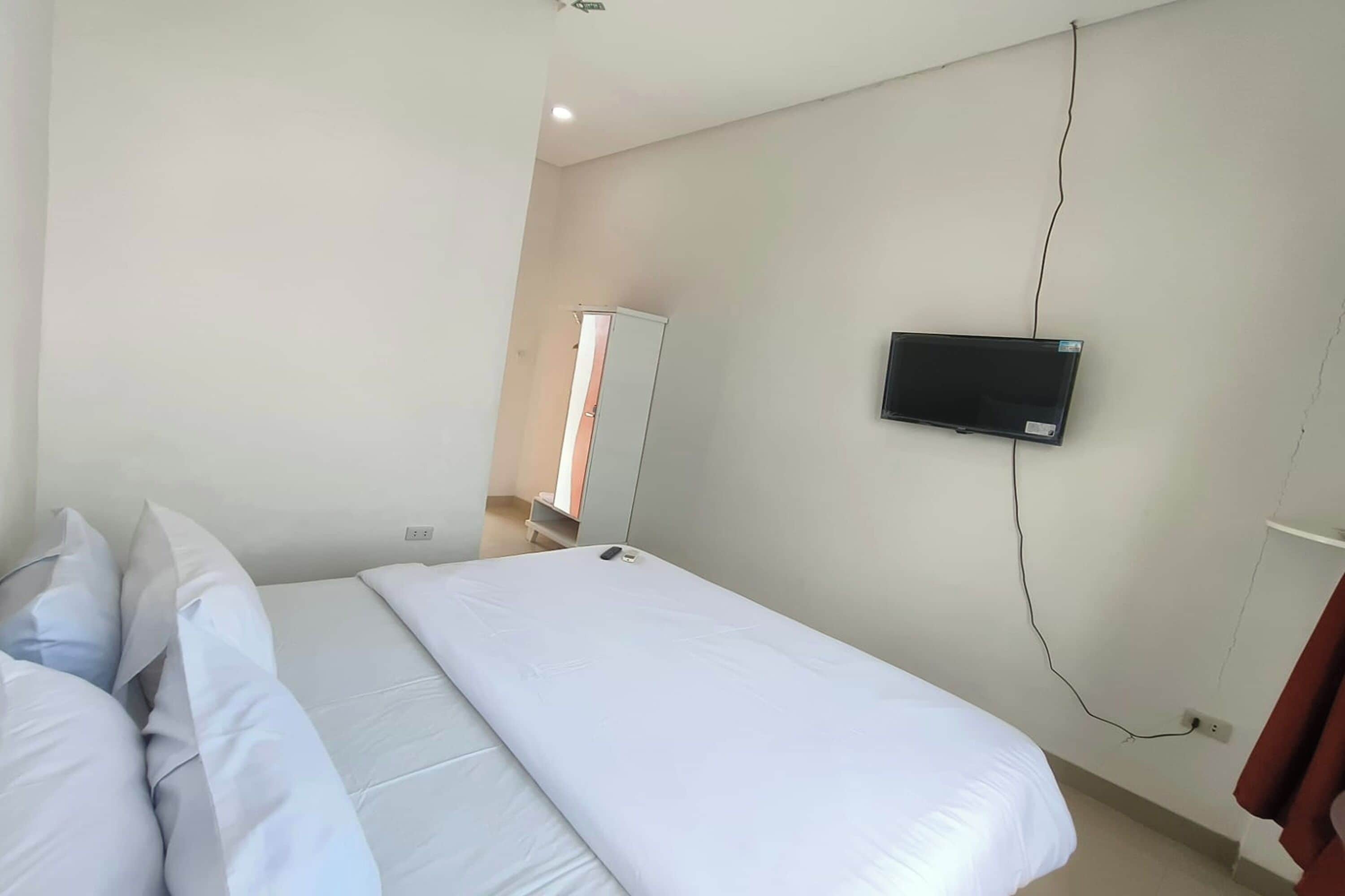 A bedroom with a bed, pillows, a TV mounted on the wall, and a wardrobe.