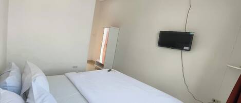 A bedroom with a bed, pillows, a TV mounted on the wall, and a wardrobe.