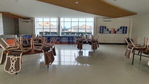 Una habitación amplia con techo alto, ventanas grandes y un área de descanso con sillas dispuestas alrededor de una mesa.