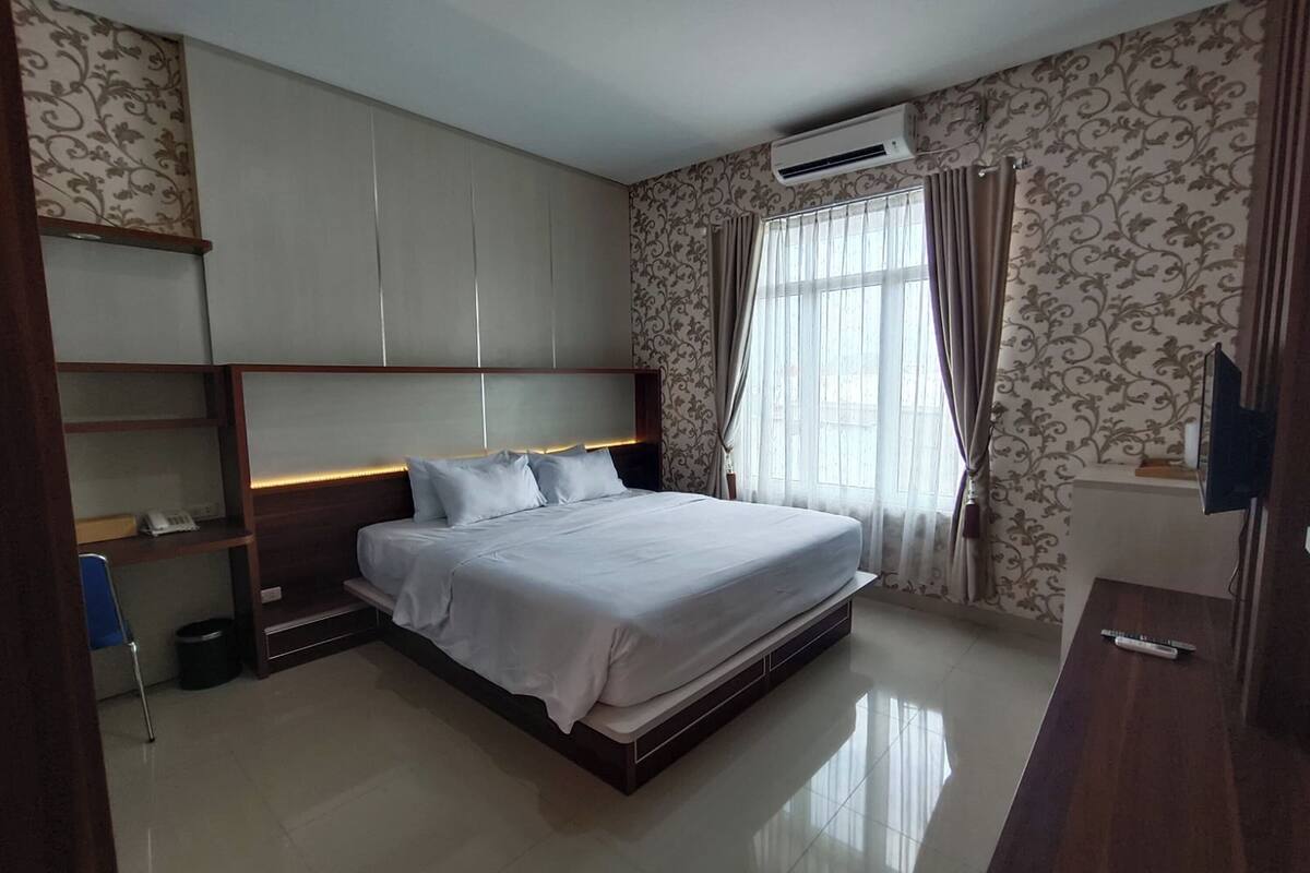 A modern bedroom with a large bed, built-in shelving, a desk, and a TV.