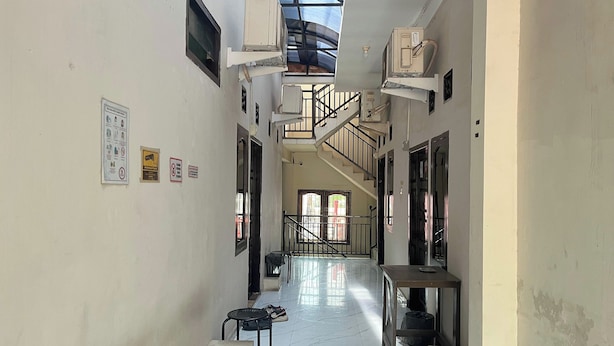 A narrow corridor with a staircase leading to an upper floor, air conditioning units mounted on the walls, and a poster on the left wall. - Pondok Family (Pangandaran)