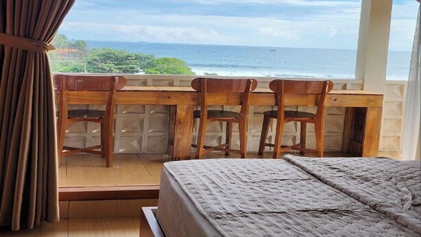Une chambre avec un grand lit, des chaises en bois et une vue sur l’océan.