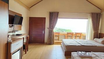 A room with a wooden ceiling, a desk with a television, two beds, and a balcony with a view.