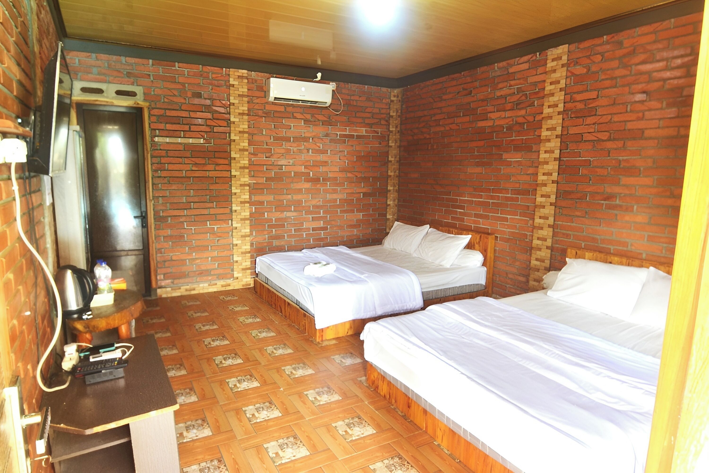 A room with two beds, a brick wall, a wooden floor, a desk, and a built-in heater.