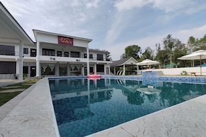 A hotel with a swimming pool, outdoor umbrellas, and a sign reading "Aden".