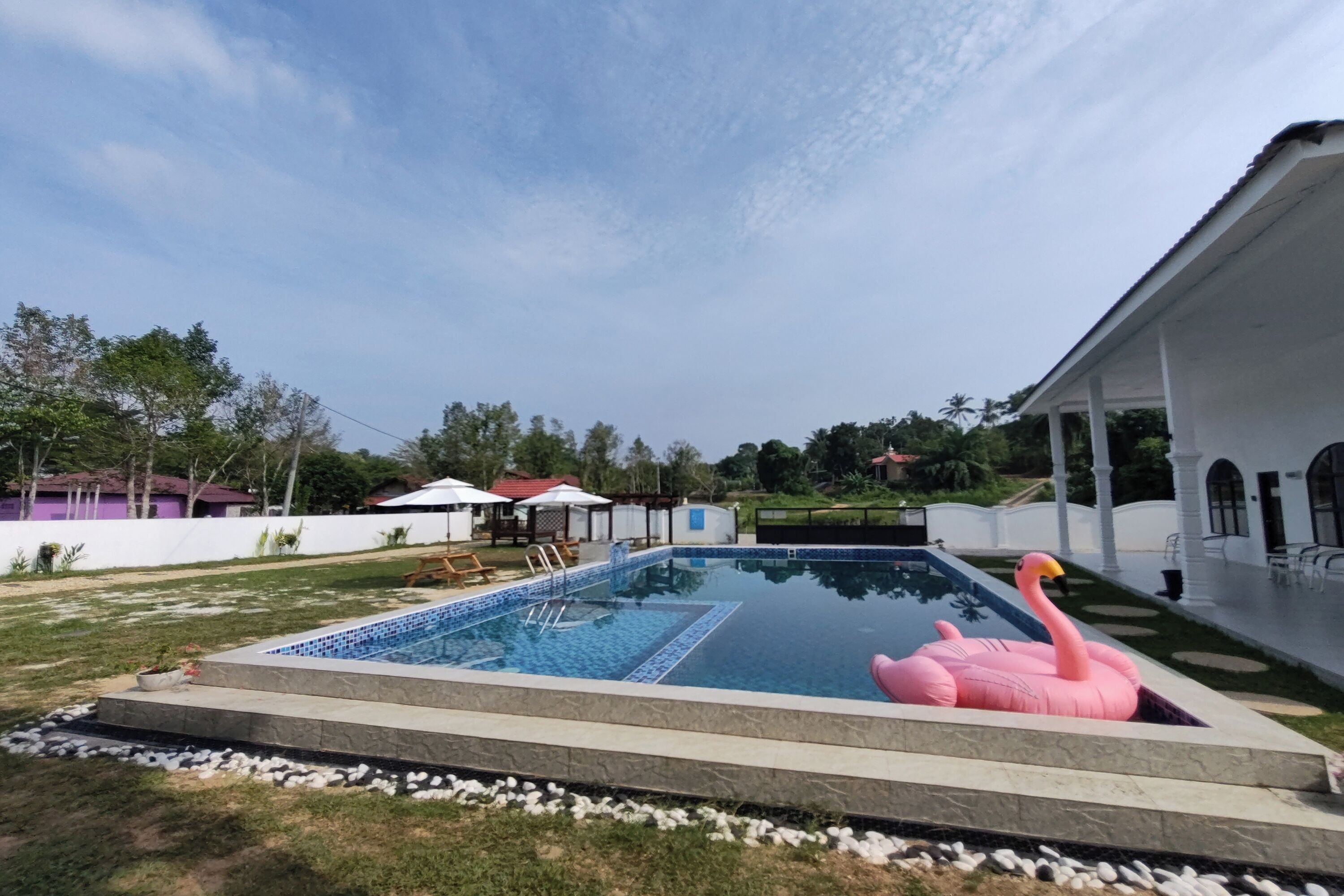 A swimming pool with a pink flamingo float, surrounded by a white building with a covered patio.