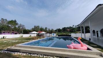 A swimming pool with a pink flamingo float, surrounded by a white building with a covered patio.