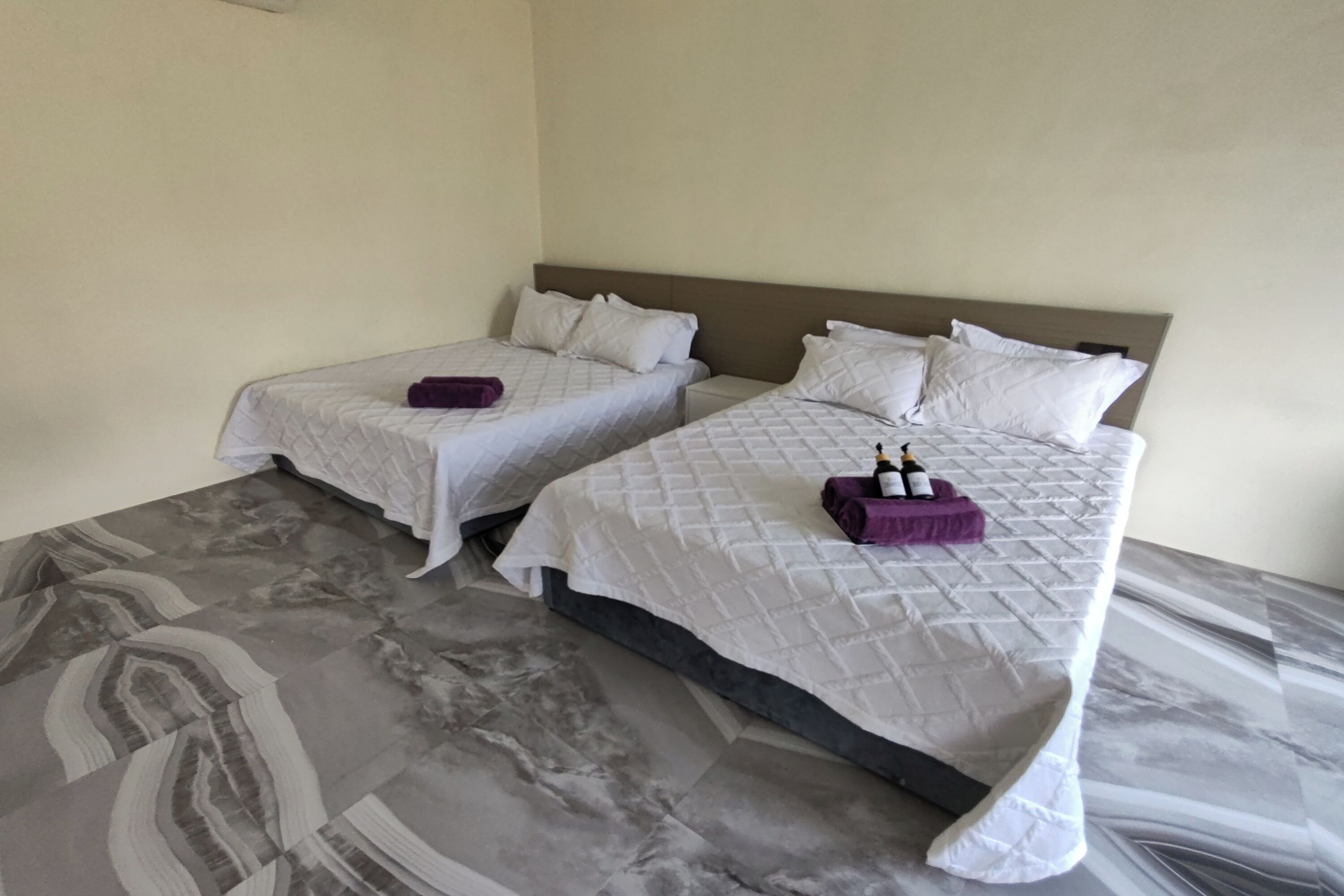 A hotel room with two beds, each with a white quilted bedspread and pillows, and a marble-patterned floor.
