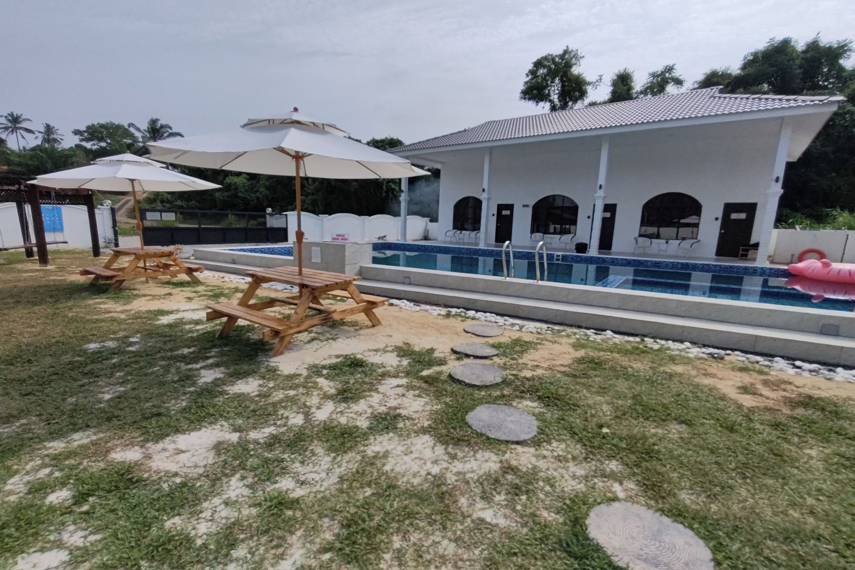 A pool area with lounge chairs and umbrellas, a swimming pool, and a building with arched windows.