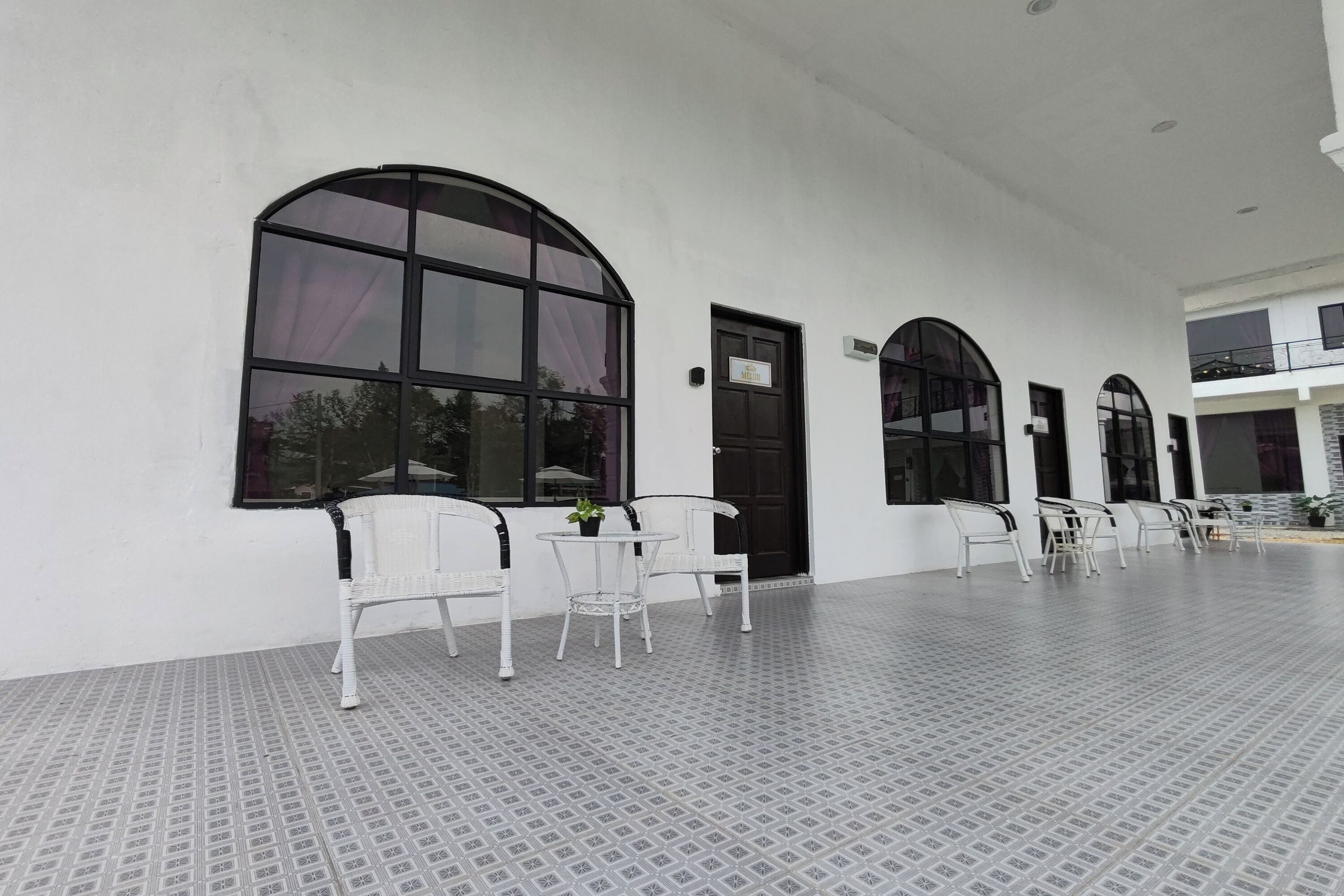 A clean, white exterior of a building with large arched windows and a tiled floor.