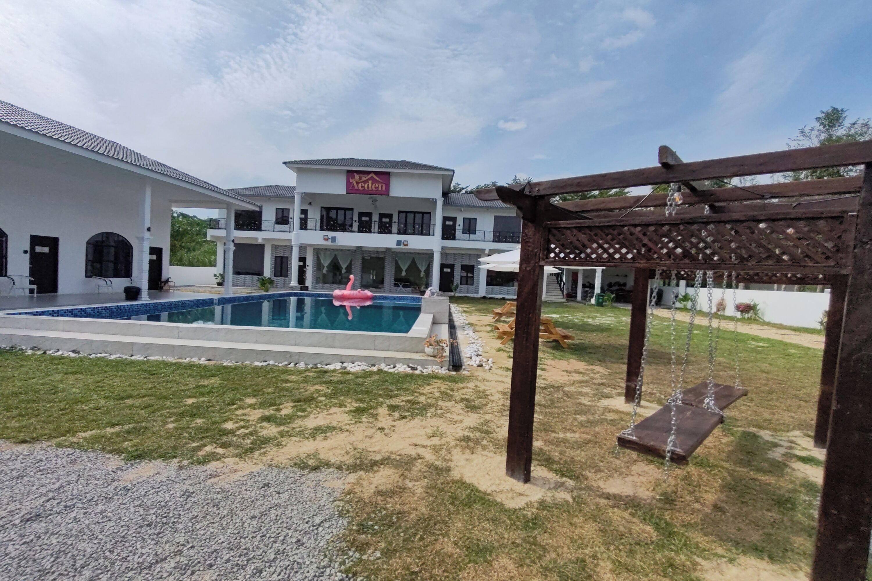 Un edificio grande con piscina, pérgola y un conjunto de columpios.