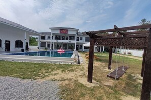 Un edificio grande con piscina, pérgola y un conjunto de columpios.