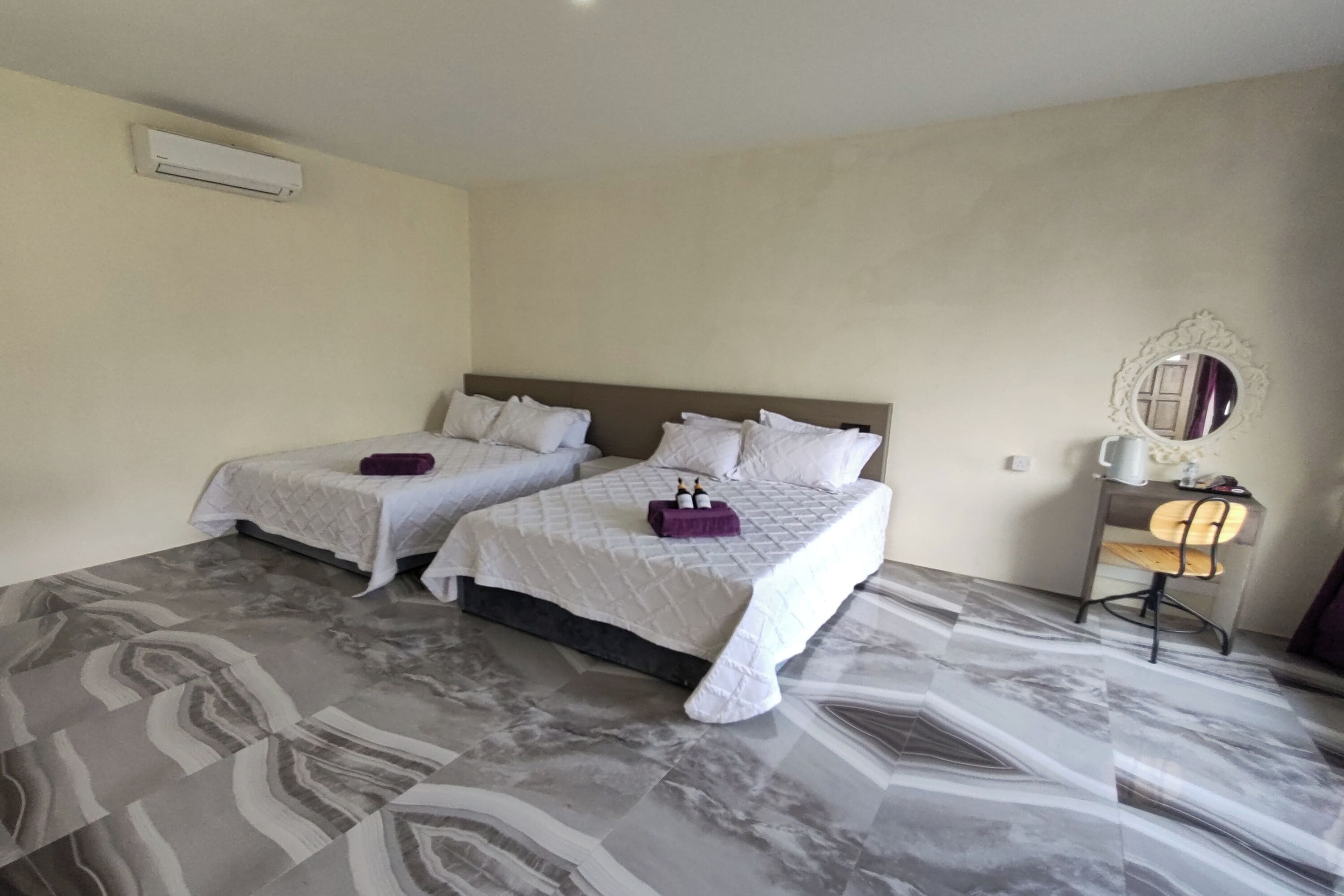 Camera d'albergo con due letti, una scrivania, una sedia e uno specchio.