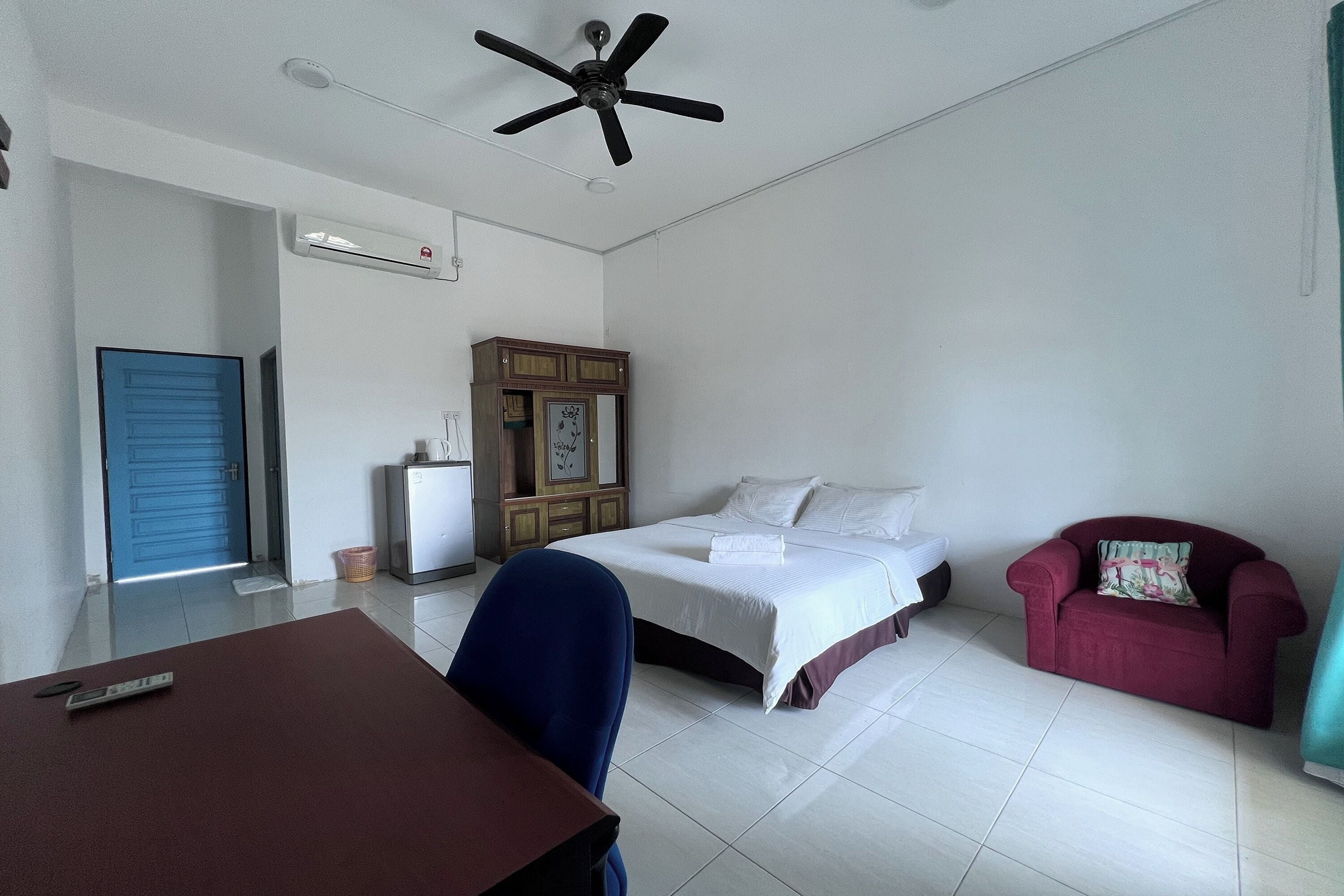 Una habitación de hotel con cama, escritorio, silla, sofá rojo, ventilador de techo y unidad de aire acondicionado.