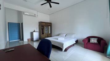 A hotel room with a bed, a desk, a chair, a red sofa, a ceiling fan, and an air conditioning unit.