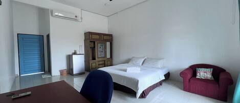 Una habitación de hotel con cama, escritorio, silla, sofá rojo, ventilador de techo y unidad de aire acondicionado.