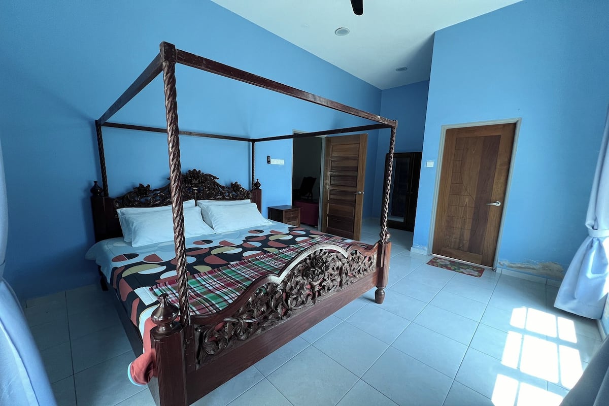 A four-poster bed with a patterned bedspread, a wooden headboard, and a nightstand with a lamp.