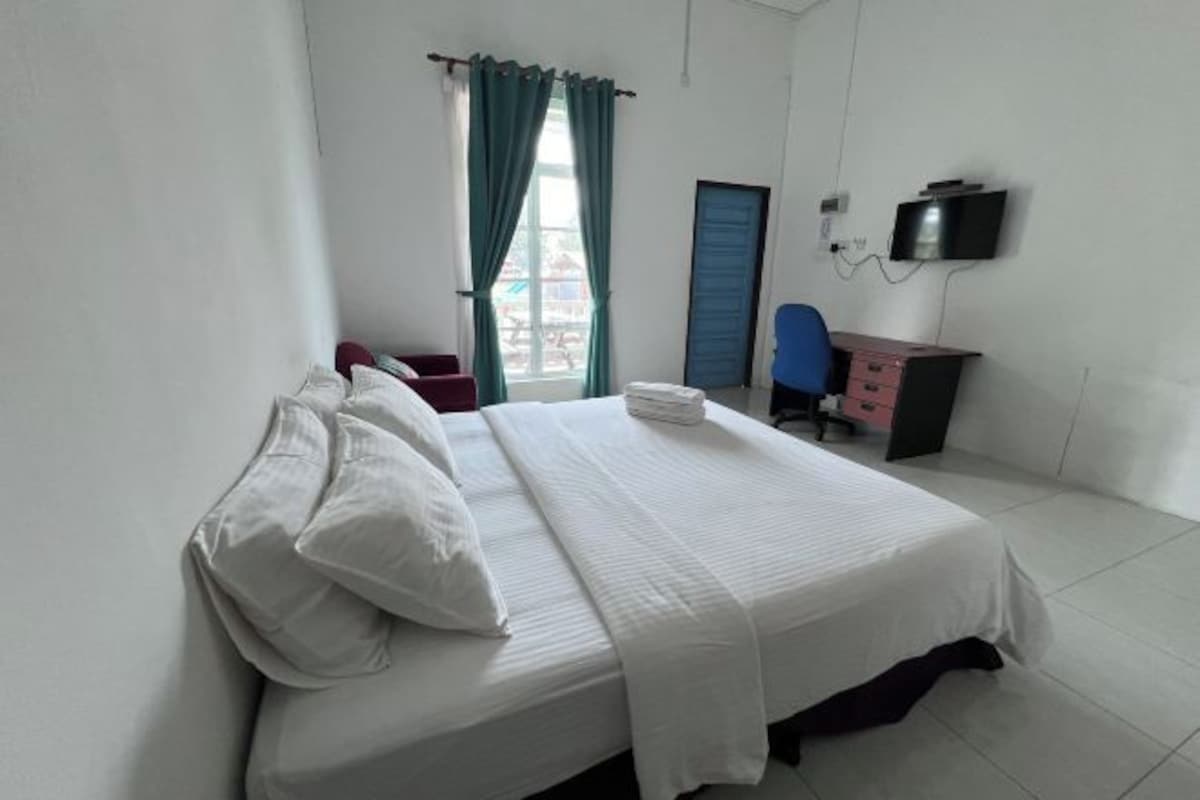 A hotel room with a bed, a desk, a chair, a TV, and a window with curtains.