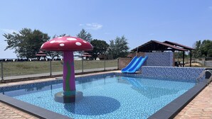 Una piscina con tobogán, una estructura con forma de hongo y una zona de estar cubierta.