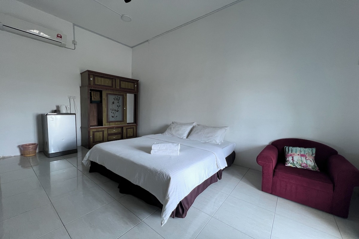 A bedroom with a bed, a wardrobe, a red armchair, and a small refrigerator.