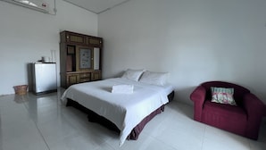 Un dormitorio con cama, armario, un sillón rojo y un refrigerador pequeño.