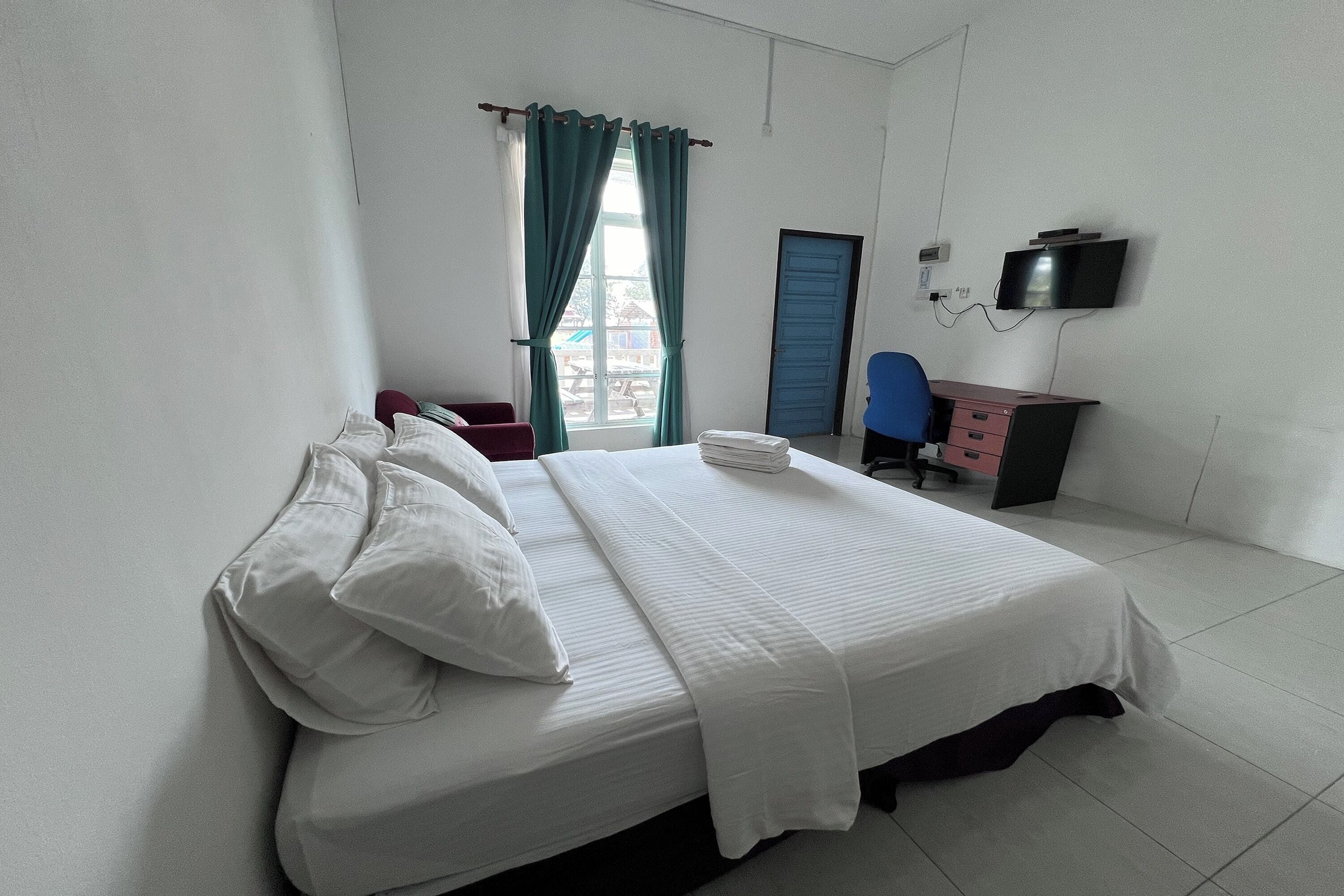 Una habitación de hotel con una cama, un escritorio, una silla, un televisor y una ventana con cortinas.