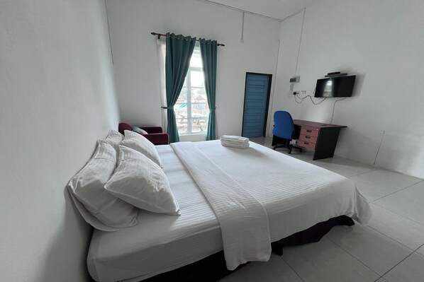 A hotel room with a bed, a desk, a chair, a TV, and a window with curtains.