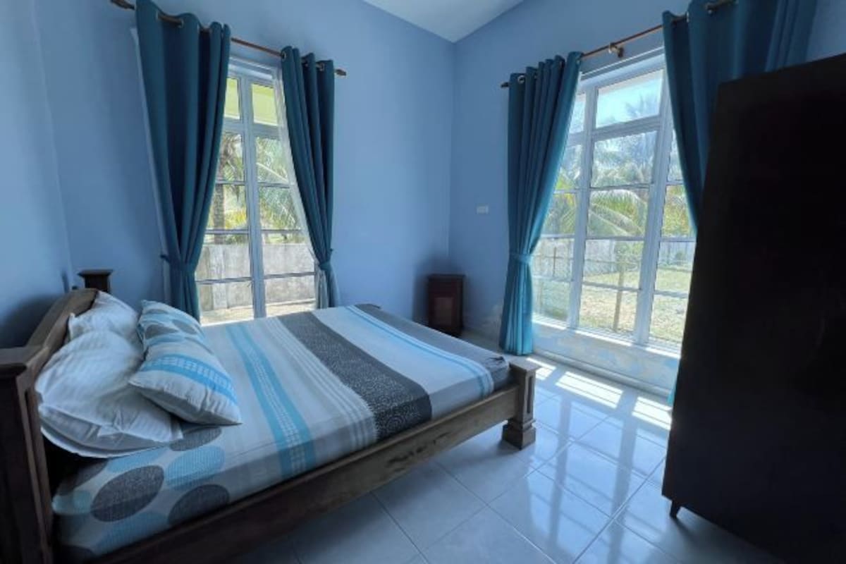 A bedroom with a bed, curtains, a window, and a view of greenery outside.