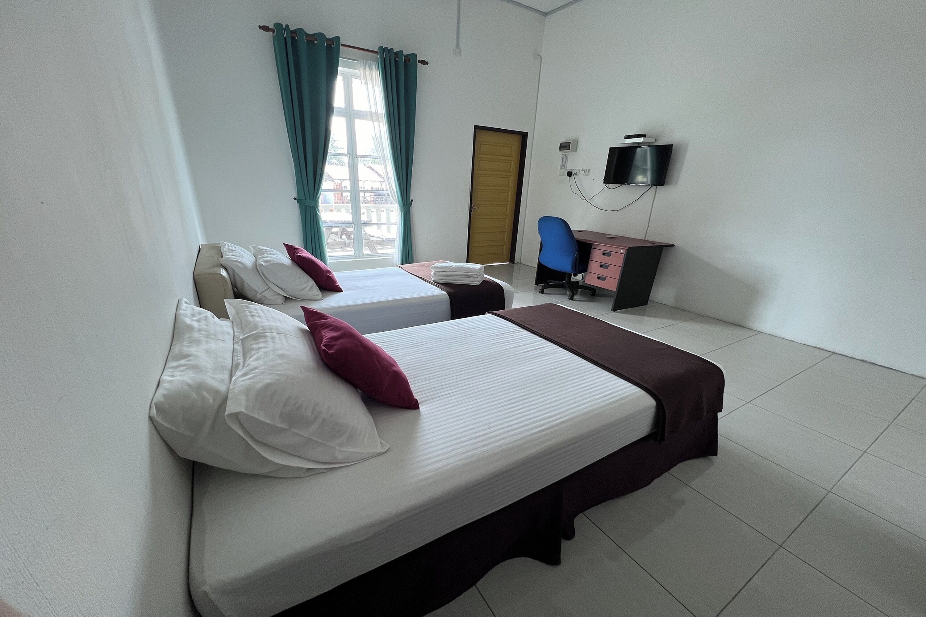Ein Hotelzimmer mit zwei Betten, einem Schreibtisch, einem Stuhl, einem Fernseher und einem Fenster mit Vorhängen.