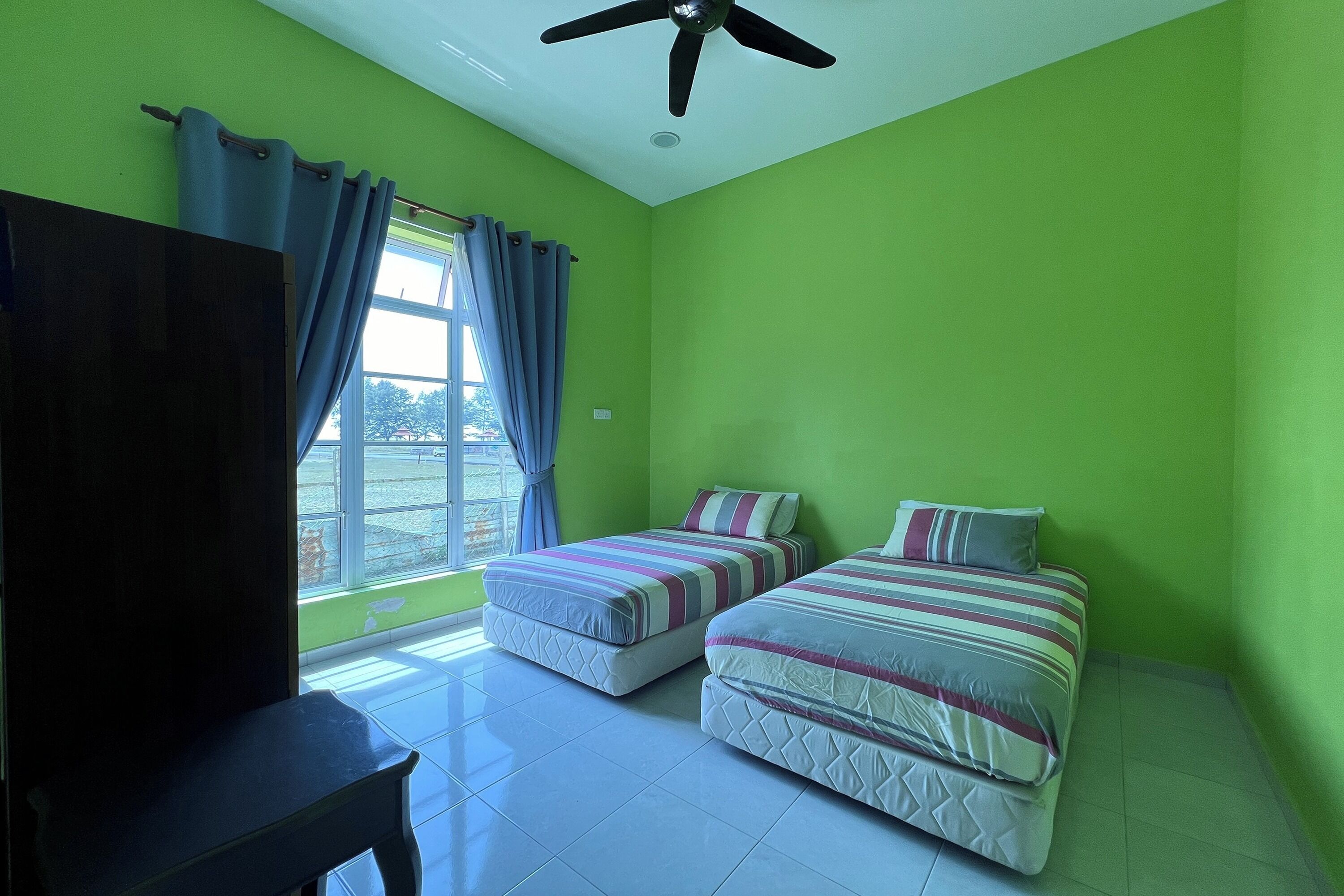 Une chambre avec deux lits, un ventilateur de plafond et une fenêtre avec des rideaux.