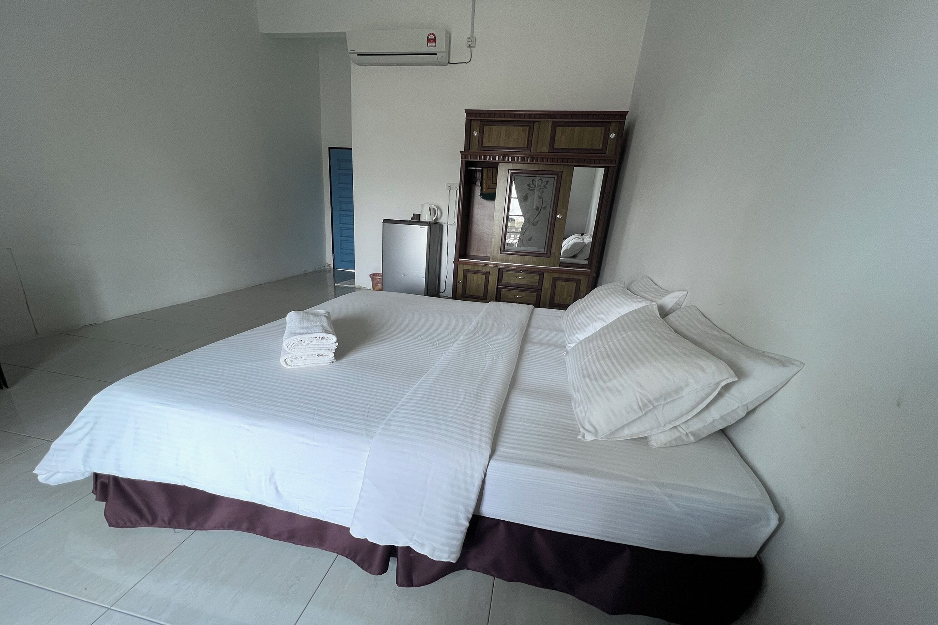 A neatly made bed with a dark skirt, a wooden headboard with a mirror, and a small table with a kettle.