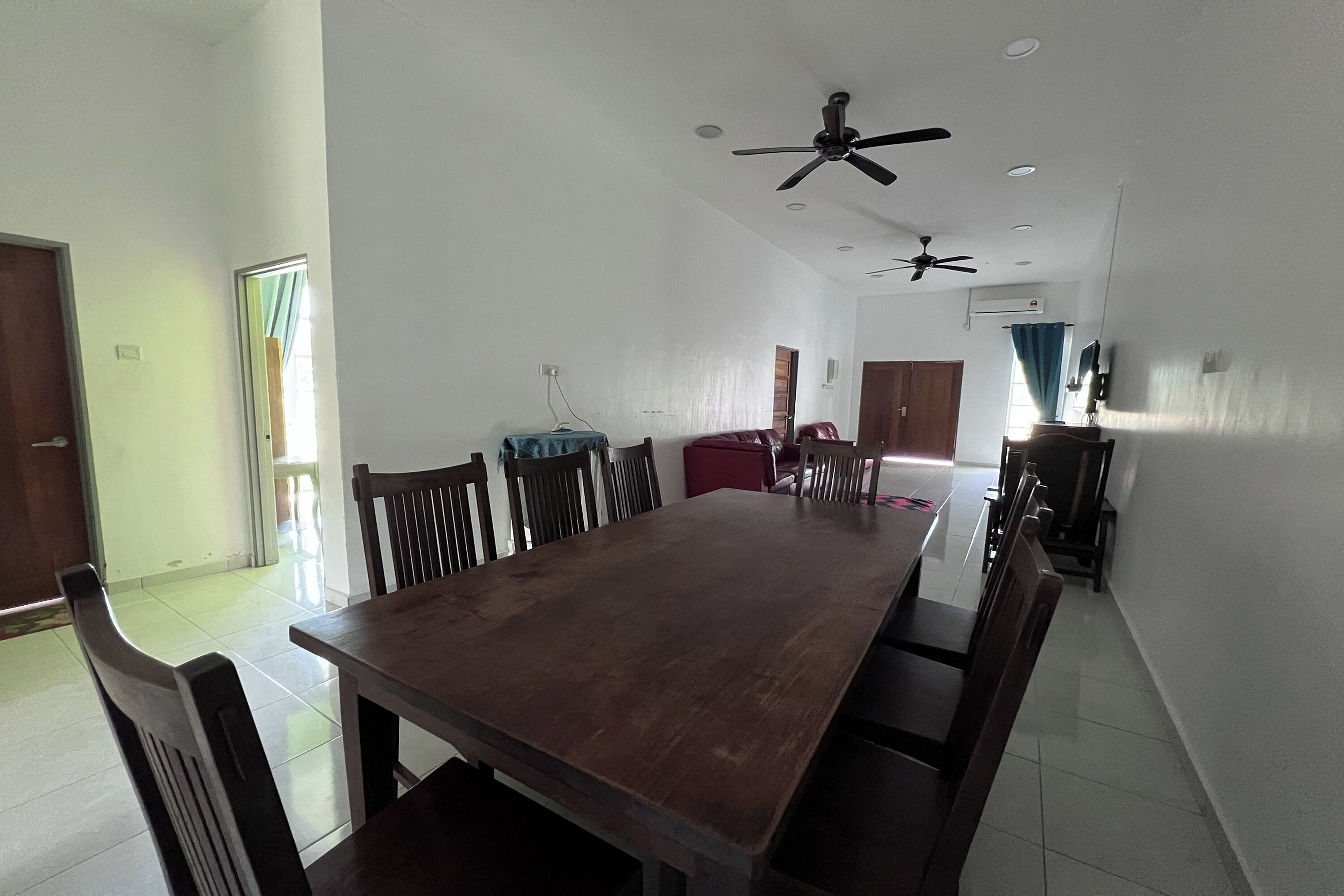 A spacious dining area with a long wooden table and chairs, ceiling fans, and a red cabinet.