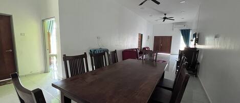 A spacious dining area with a long wooden table and chairs, ceiling fans, and a red cabinet.