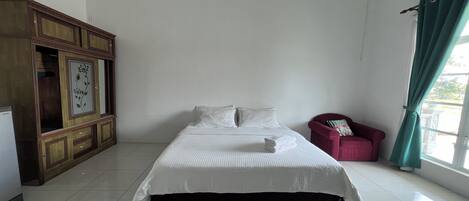 A neatly made bed in a room with a wooden cabinet and a red chair.