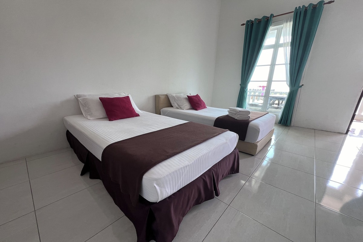 A hotel room with two beds, each with a white mattress and maroon bedding.