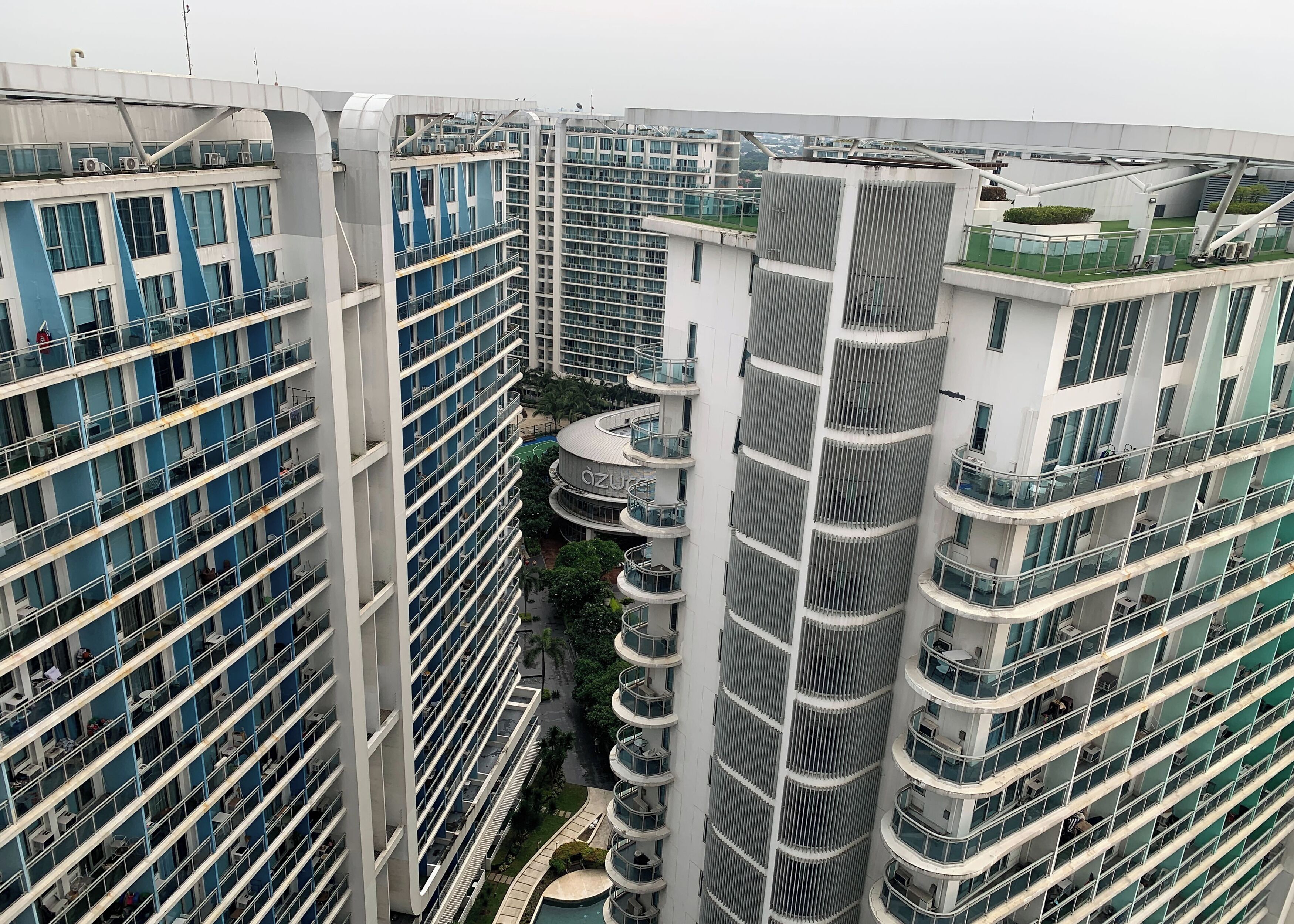 A high-rise building with multiple balconies, a central courtyard, and a pool area.