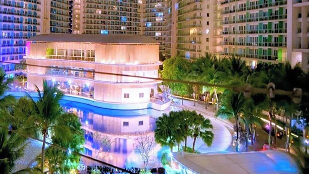 A high-rise hotel with multiple balconies, a central pool area, and lush landscaping. - Budget Suite Paranaque (Parañaque)