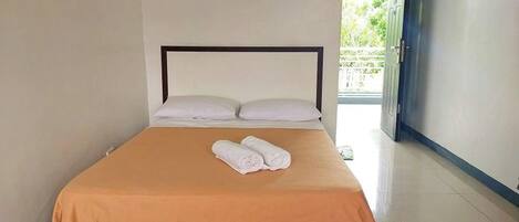 A neatly made bed with a brown bedspread and white pillows, a pair of rolled towels on the bed, and a small sign on the wall above the bed.