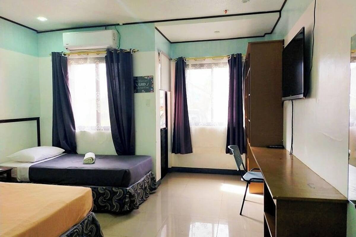 A hotel room with two beds, a desk, a chair, and a TV.