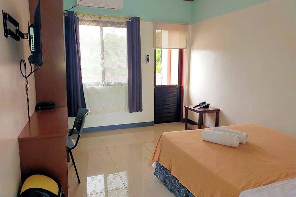 A hotel room with a bed, a desk, a chair, a telephone, and a window with curtains.