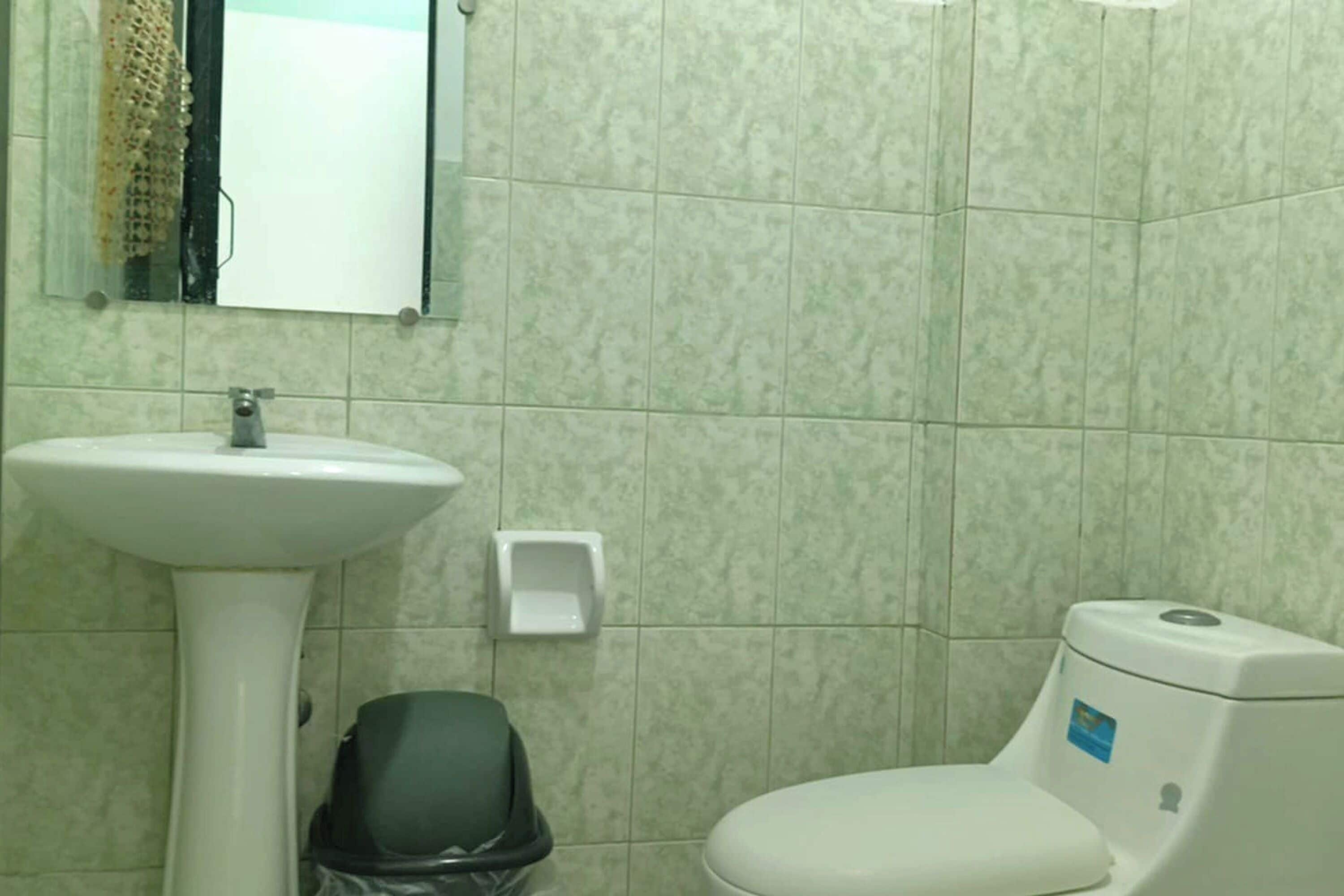 A bathroom with a pedestal sink, a toilet, and a trash bin.