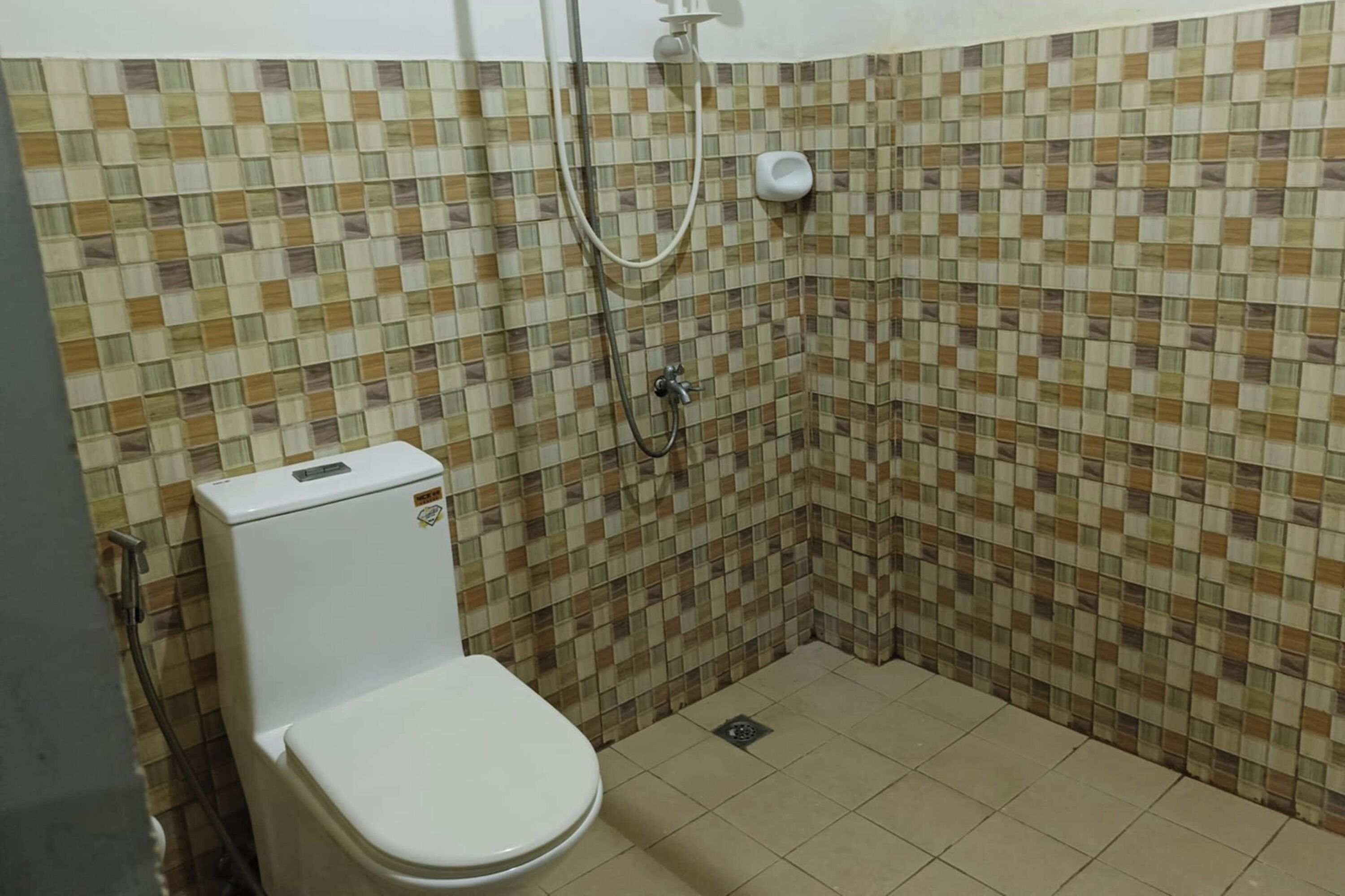 A small, tiled bathroom with a toilet, a shower, and a toilet paper holder.