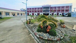 A building with a red and white facade, multiple balconies, and a landscaped garden with palm trees and potted plants. - EC Hotel near Laoag Airport (Laoag)