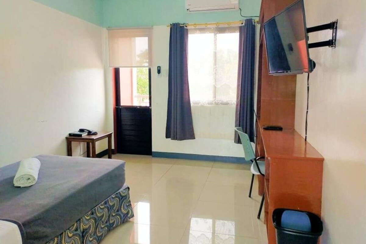 A room with a bed, a desk, a chair, a TV, and a window with curtains.