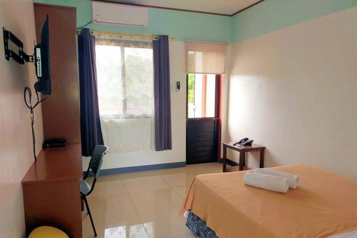 A hotel room with a bed, a desk, a chair, a television, and a window with curtains.